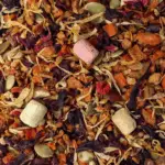 Infusion d'Halloween : Photo de l'infusion vue de haut. Tous les ingrédients sont visibles dans un mélange multicolore : carotte, hibiscus, chamallows, noisettes...